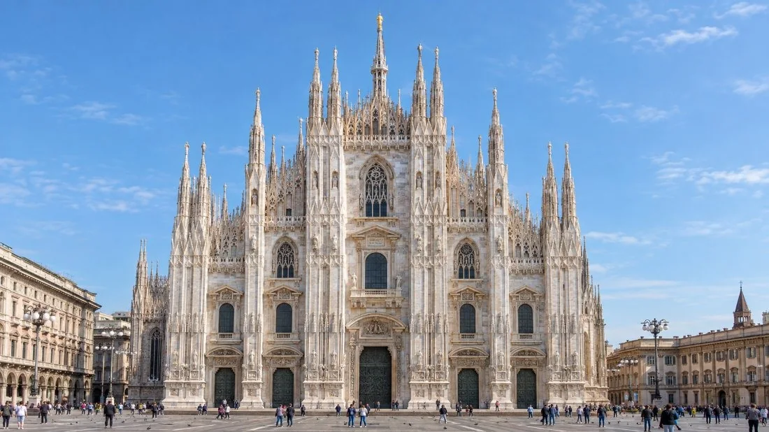 The marble facade of the Duomo di Milano with its five bronze doors and statues, seen from Piazza del Duomo in morning light