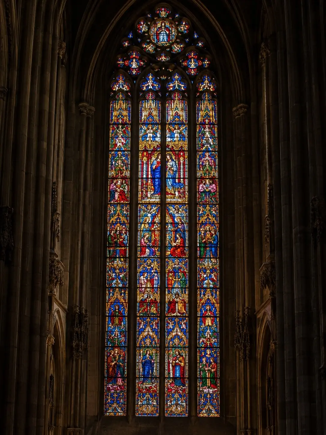 A monumental stained-glass window of the Duomo di Milano apse glowing in red, blue and gold