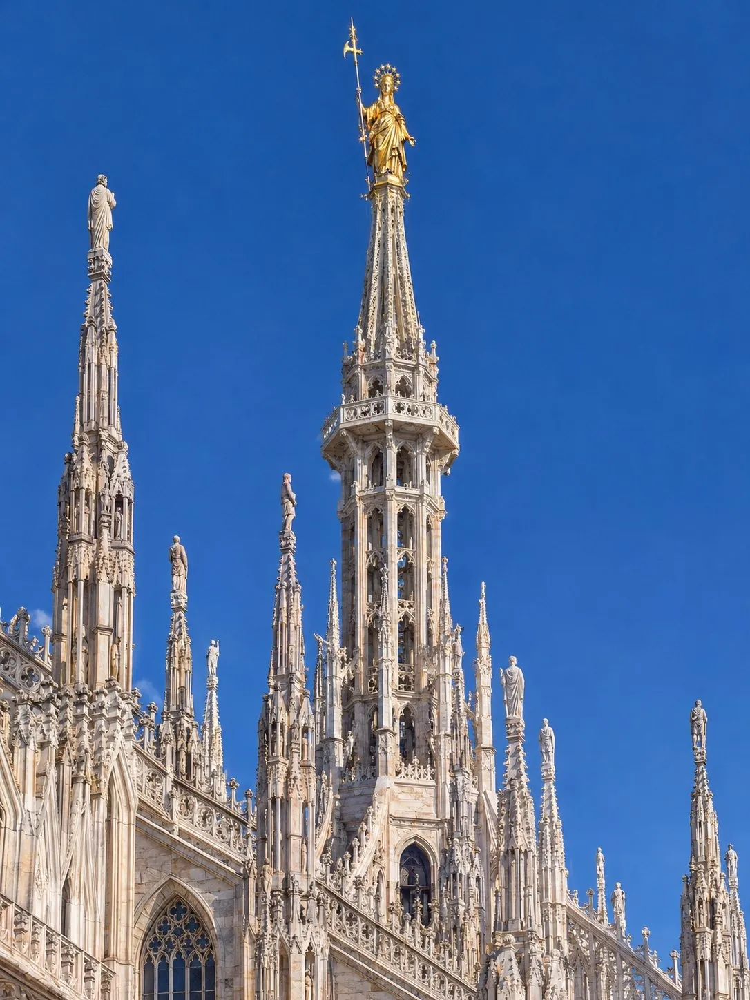 The golden Madonnina on the main spire of the Duomo, seen from the highest terrace against a blue sky